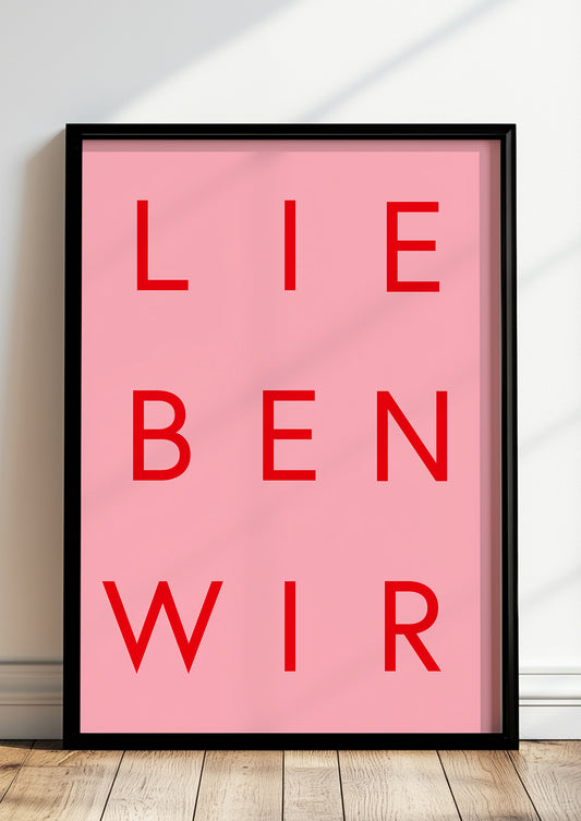 Rotes Typografieposter „LIEBEN WIR“ im schwarzen Holzrahmen, stehend auf dem Boden
