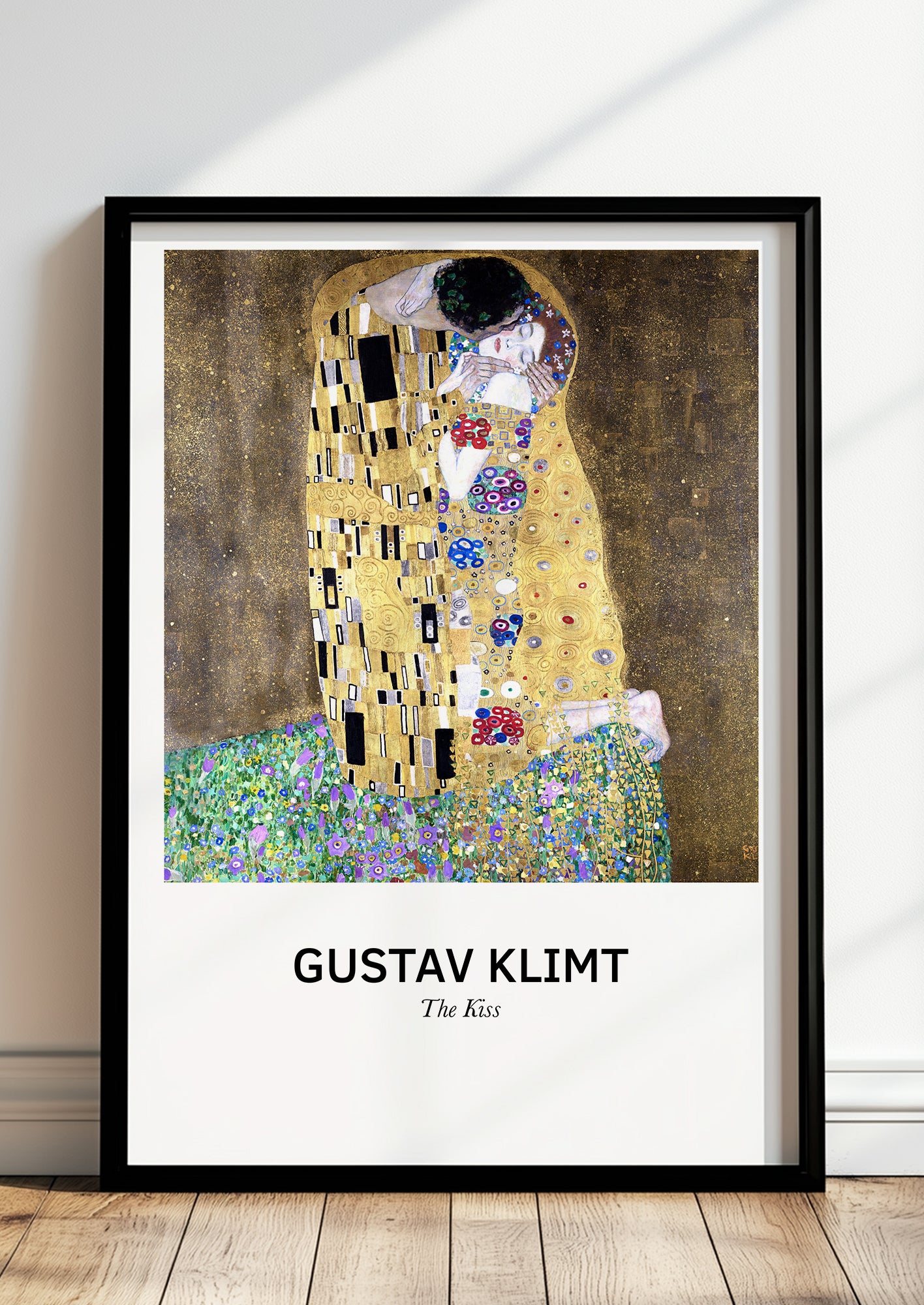 The Kiss von Gustav Klimt als Poster, in schwarzem Rahmen, stehend auf dem Boden, angelehnt an einer Wand