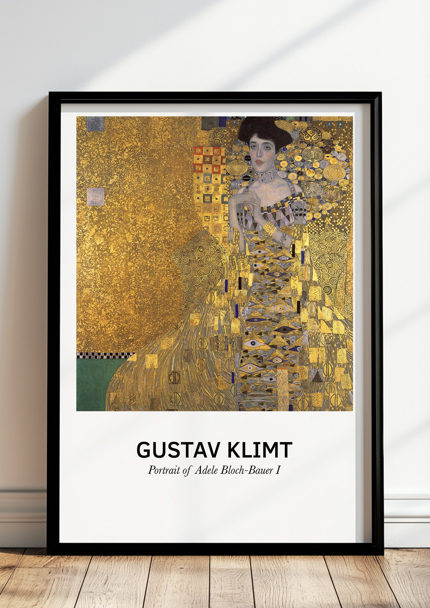 Portrait of Adele Bloch-Bauer I von Gustav Klimt als Poster, in schwarzem Rahmen, stehend auf dem Boden, angelehnt an einer Wand