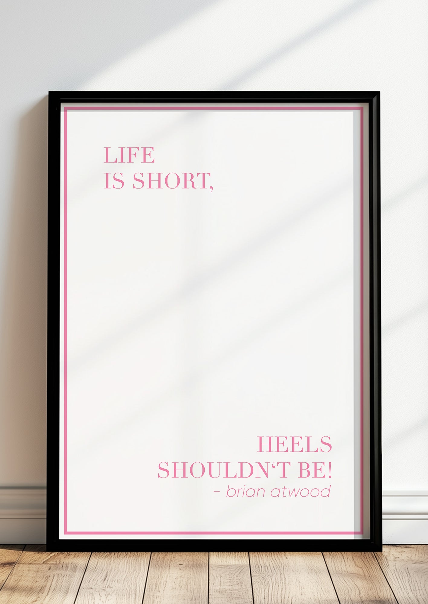 Zitatposter „Life is short, heels shouldn’t be!“ in schwarzem Holzrahmen steht auf dem Boden