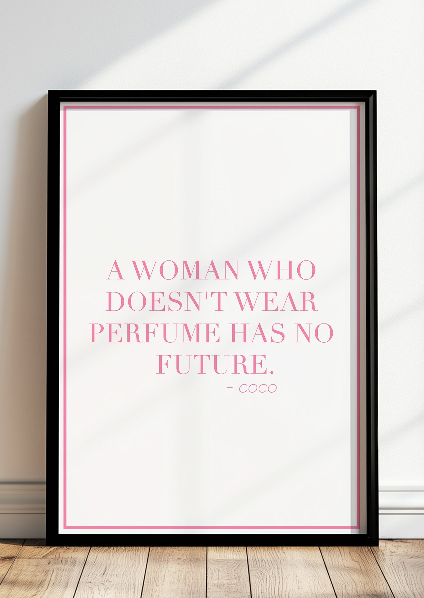 Zitatposter "A woman who doesn’t wear perfume has no future." in schwarzem Holzrahmen steht auf dem Boden