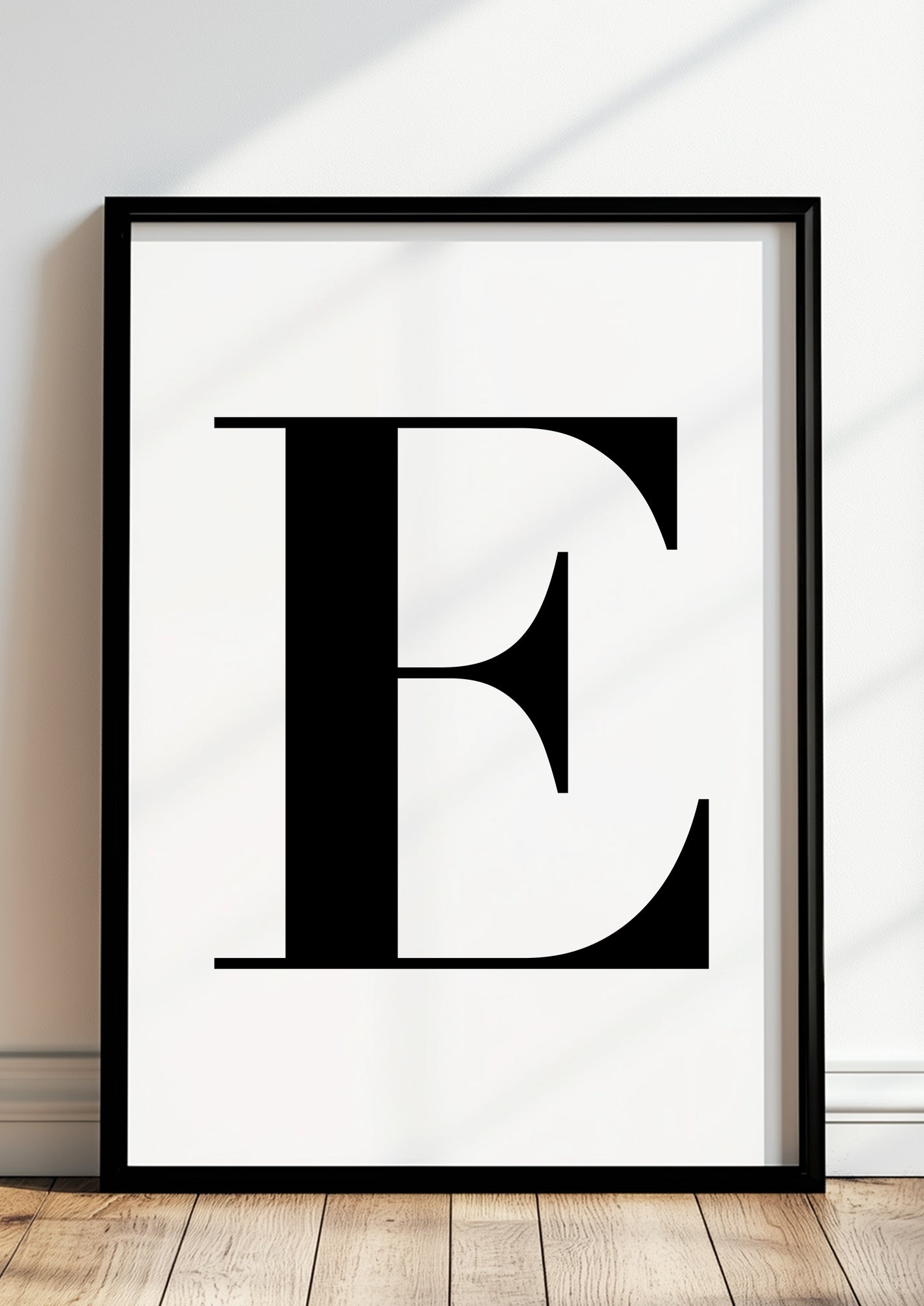 Poster Buchstabe „E“ in schwarzem Holzrahmen steht auf dem Boden