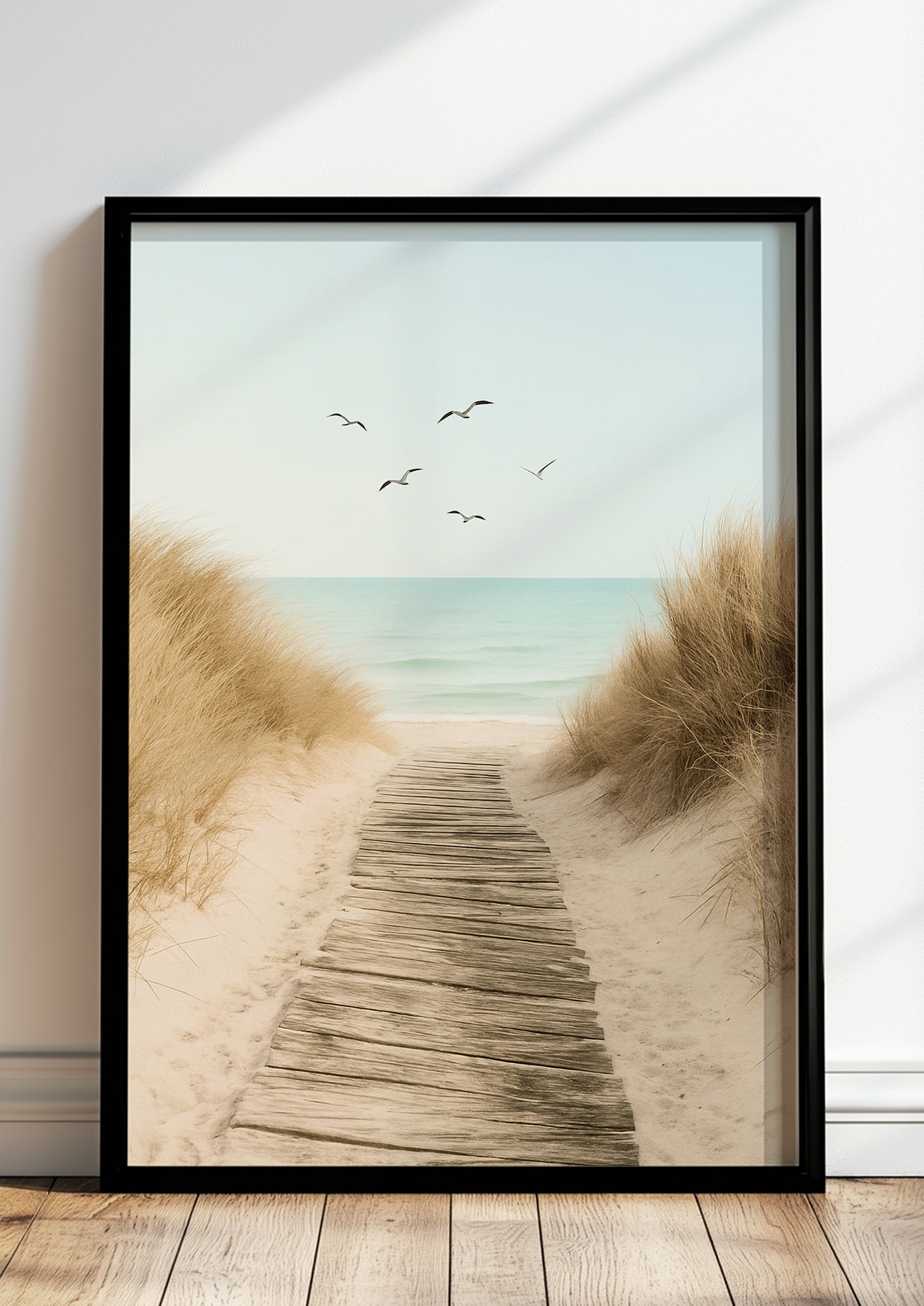 Fotoposter mit Strandweg im schwarzen Rahmen vor heller Wand mit Naturdeko