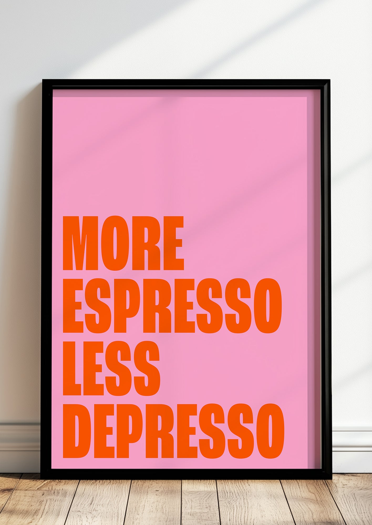 Gerahmtes Poster mit dem Schriftzug „More Espresso Less Depresso“ lehnt auf dem Boden vor einer Wand
