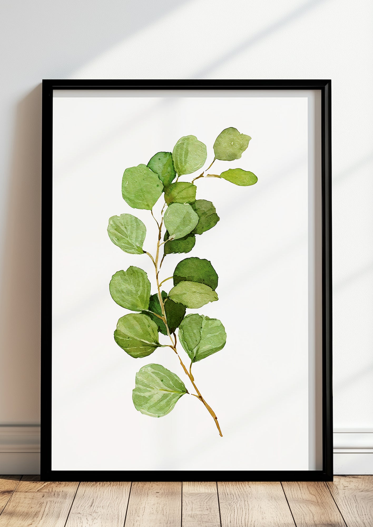 Gerahmtes Poster mit Silver Dollar Eukalyptuszweig lehnt auf dem Boden vor einer hellen Wand