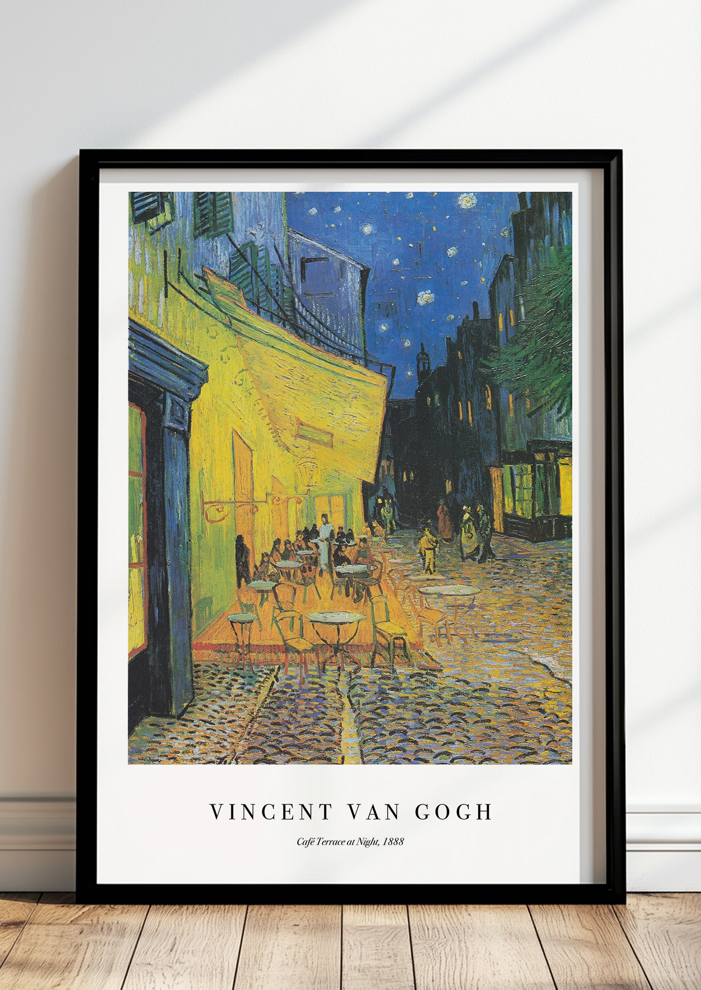 Café Terrace at Night von Vincent van Gogh als Poster, in schwarzem Rahmen, stehend auf dem Boden, angelehnt an einer Wand