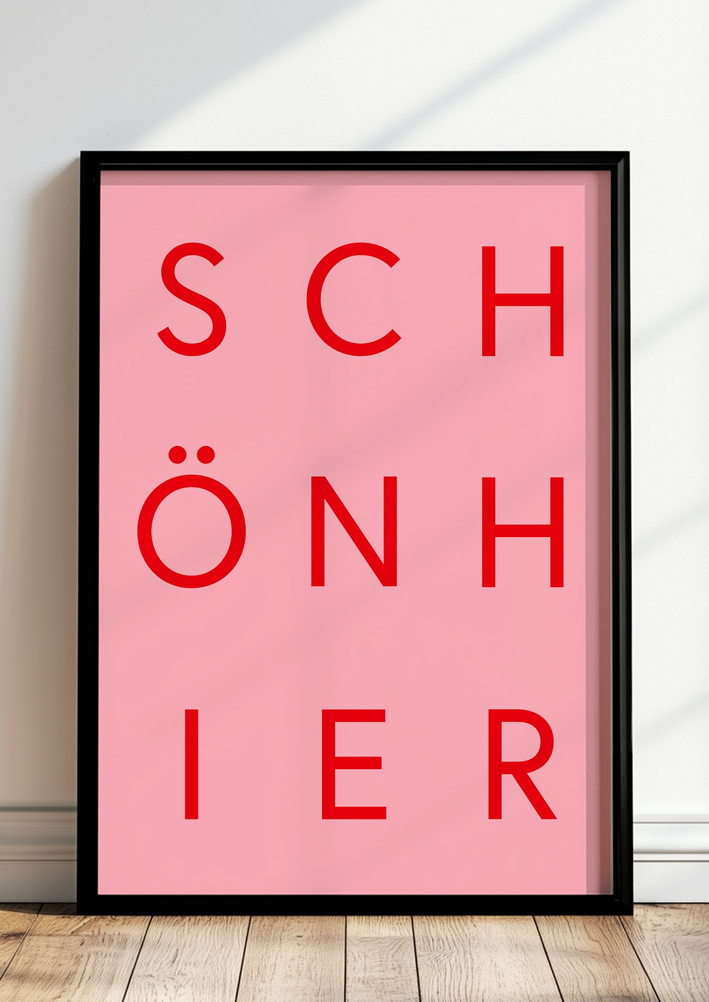 Typografieposter „SCHÖN HIER“ in roter Schrift im schwarzen Holzrahmen, stehend auf dem Boden