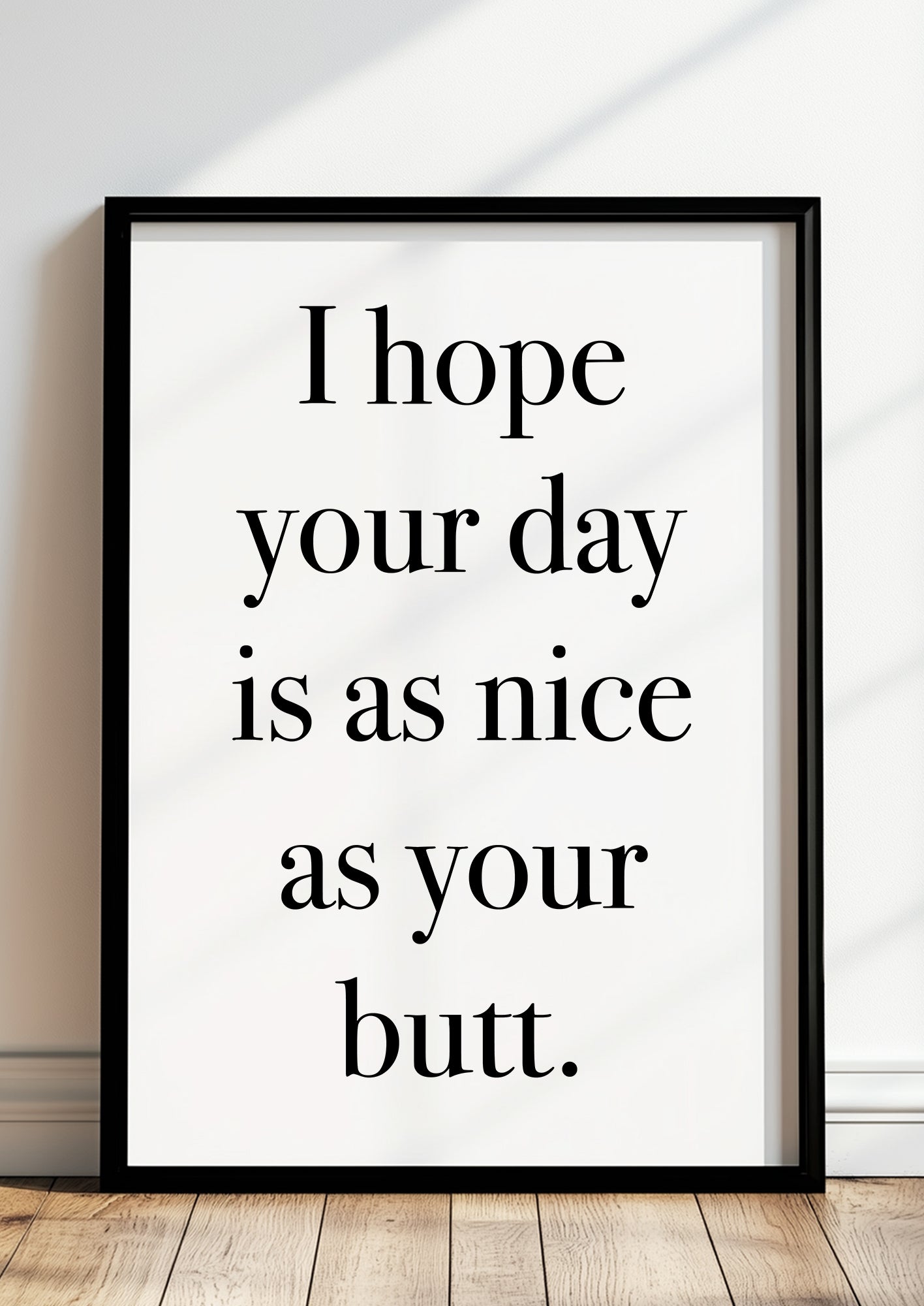 Gerahmtes Poster „I hope your day is as nice as your butt.“ in schwarzem Rahmen, inszeniert in moderner Wohnumgebung.