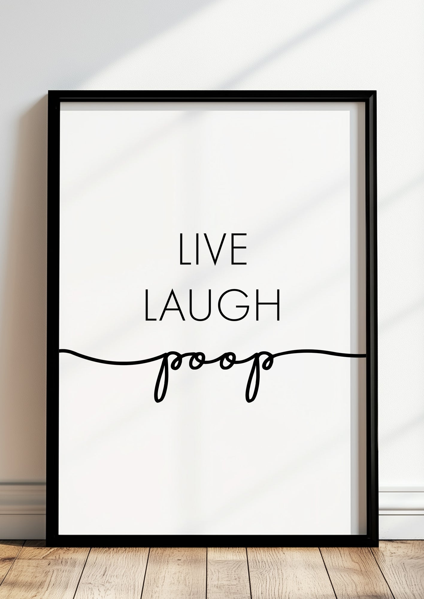 Witziges Typografie-Poster ‚Live Laugh Poop‘ in elegantem schwarzen Rahmen, stehende Darstellung auf Holzfußboden – perfekte Dekoidee für moderne Badezimmer oder Gäste-WCs